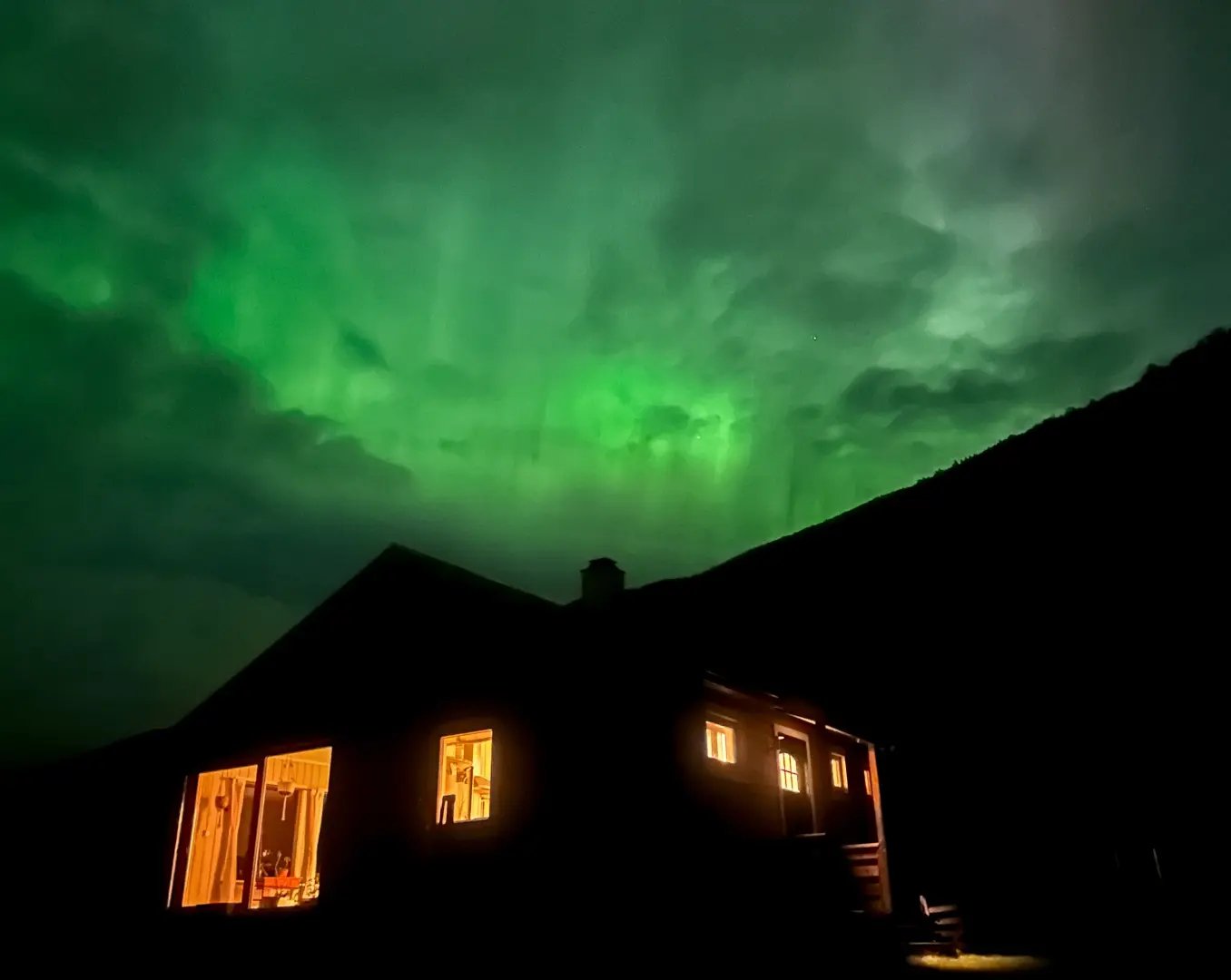 Northern Lights in the best time to see them in Norway, December, above a cabin with tourists
