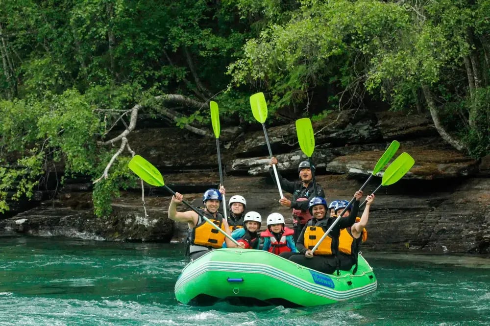 people enjoying a family rafting adventure on a clear turquoise river surrounded by lush green forest, raising their paddles and smiling