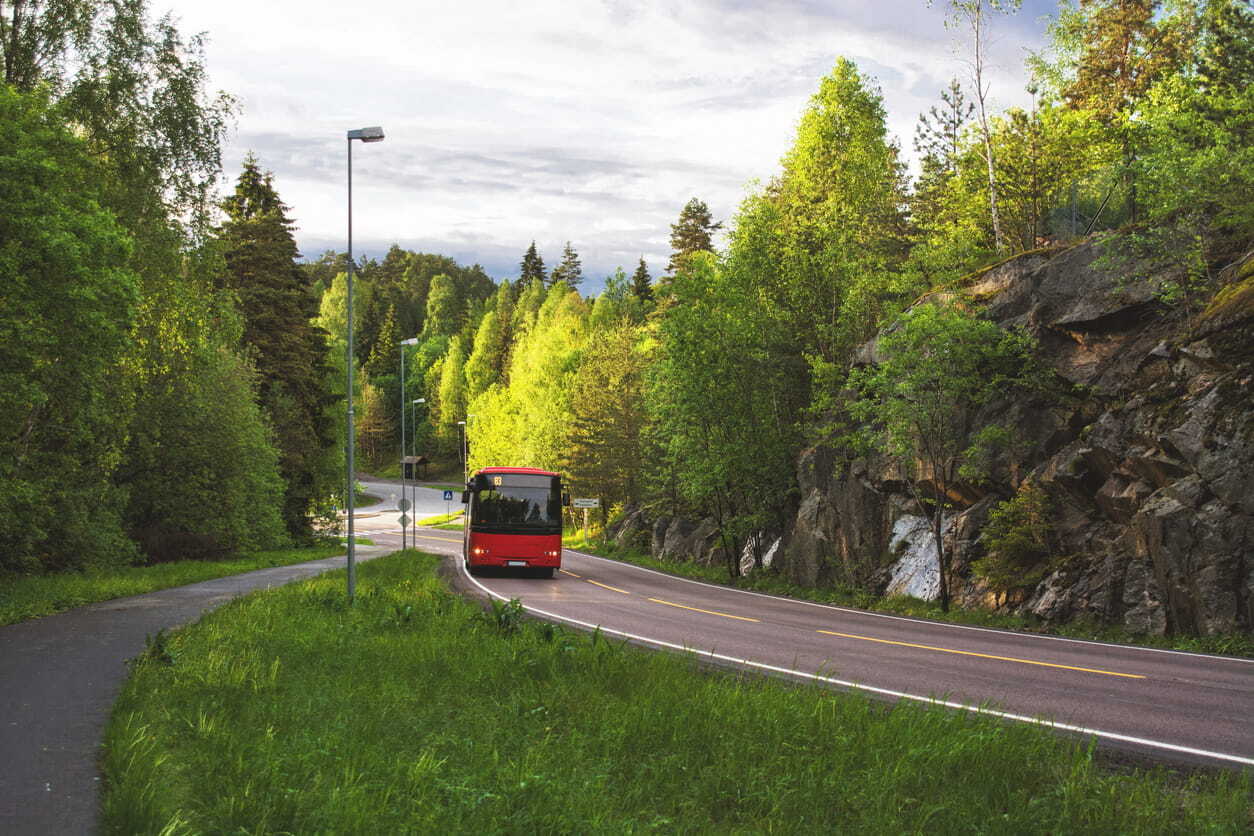 A bus driving from Oslo to Bergen along a forested road