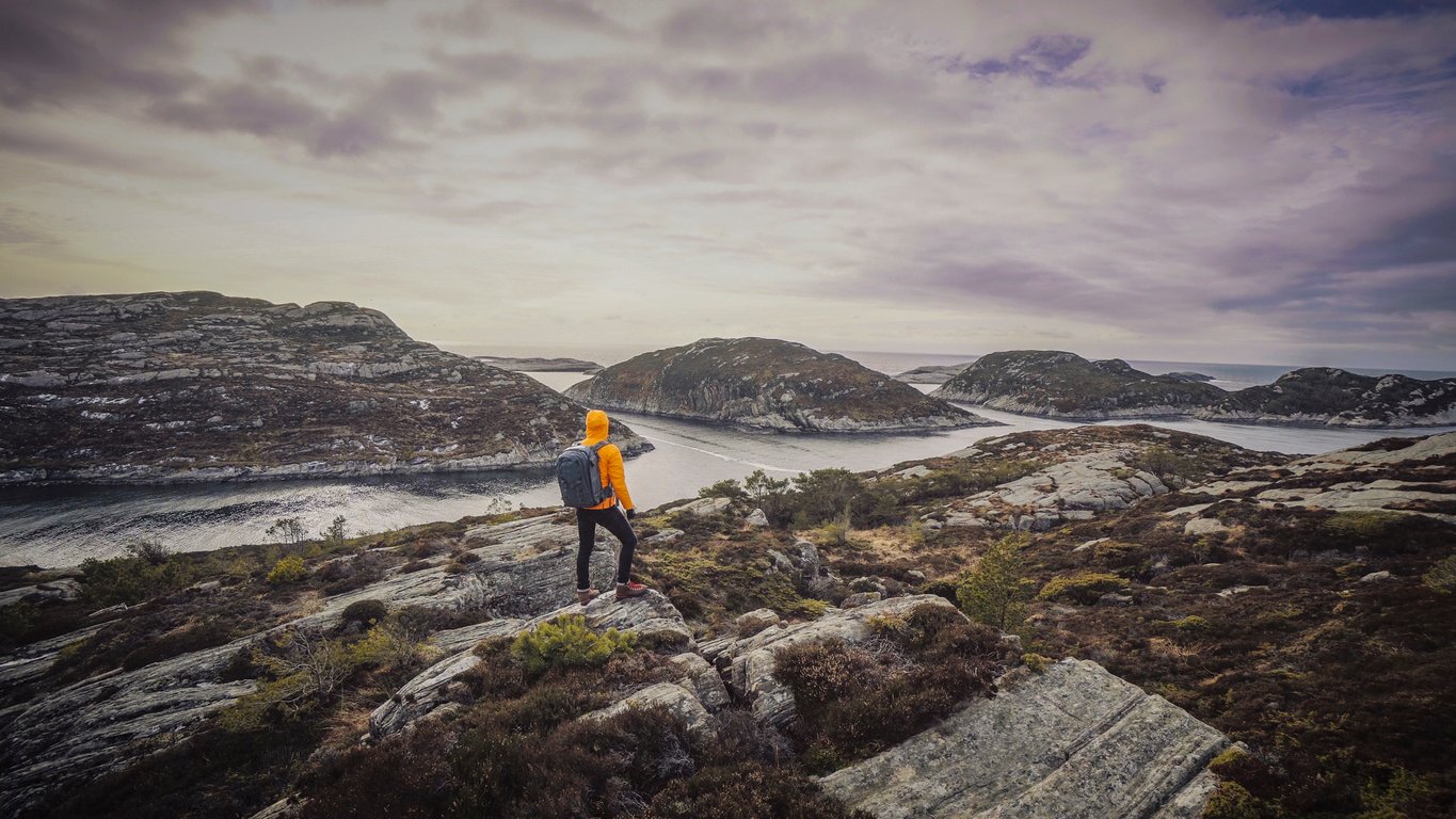 Hiker wearing a yellow jacket hiking among the fjords of Bergen, Norway