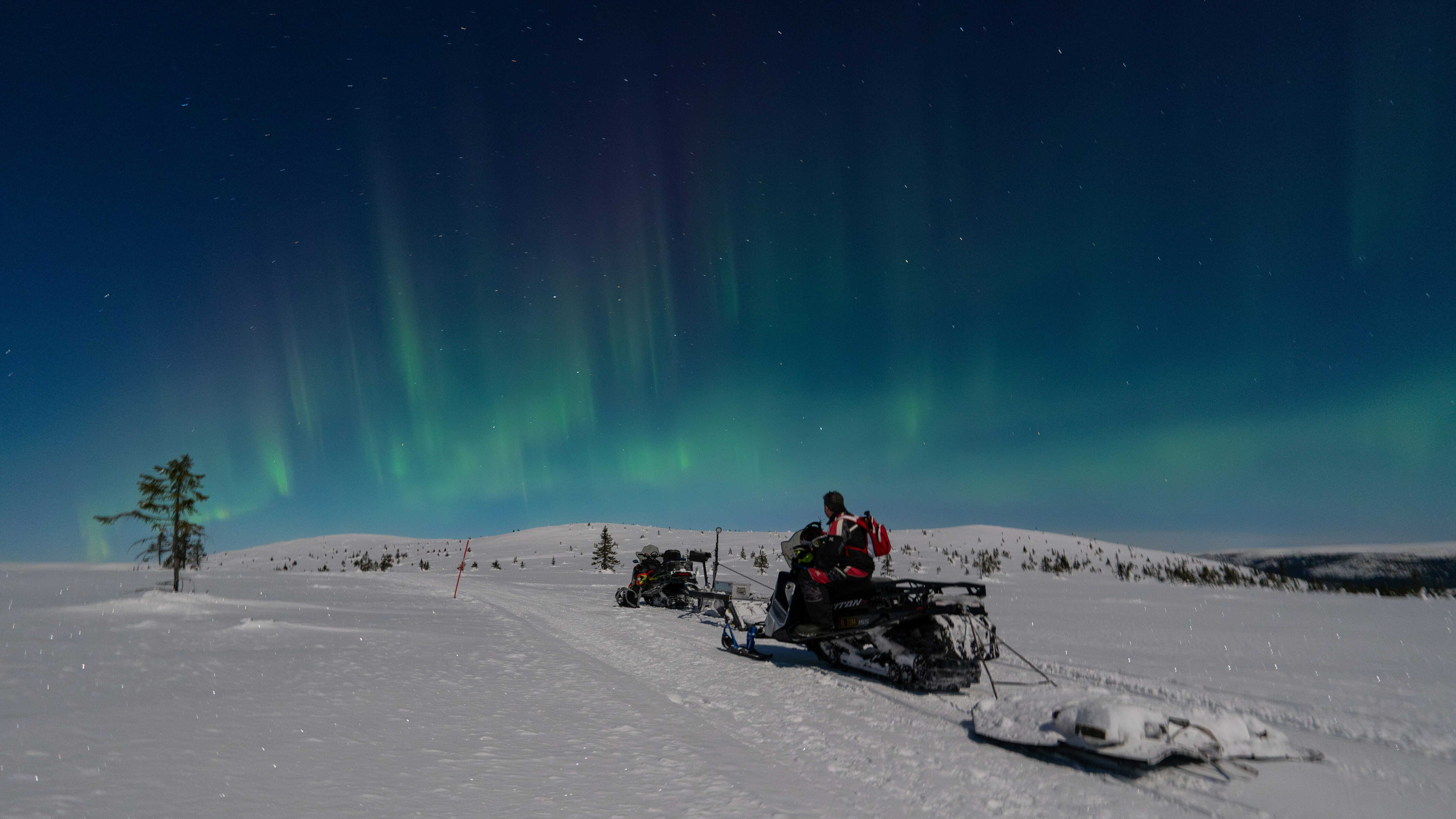 A man skimobiling under the Northern Lights in Norway