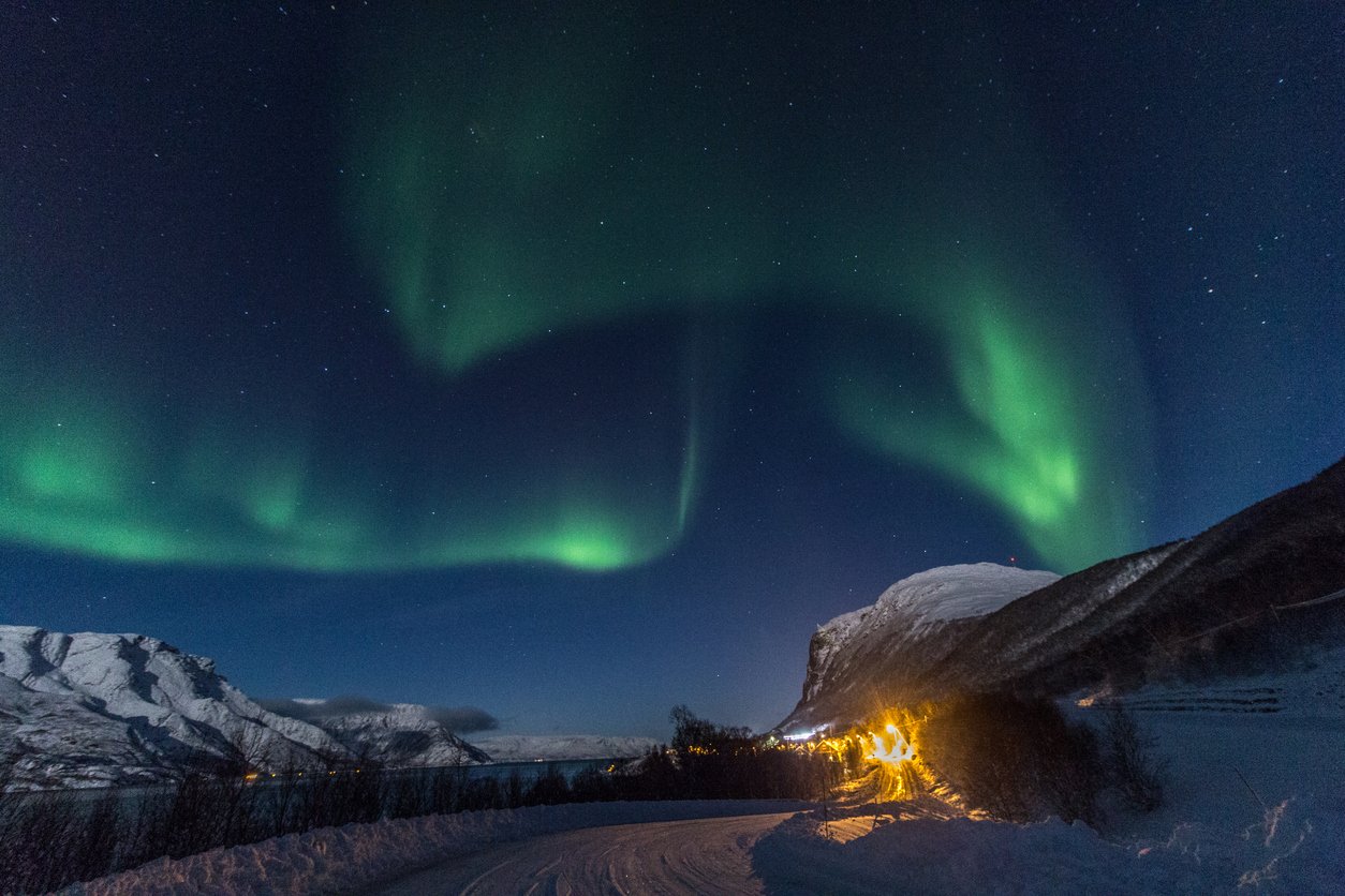 A view of the Northern Lights shining above Alta, Norway, and a snowy road