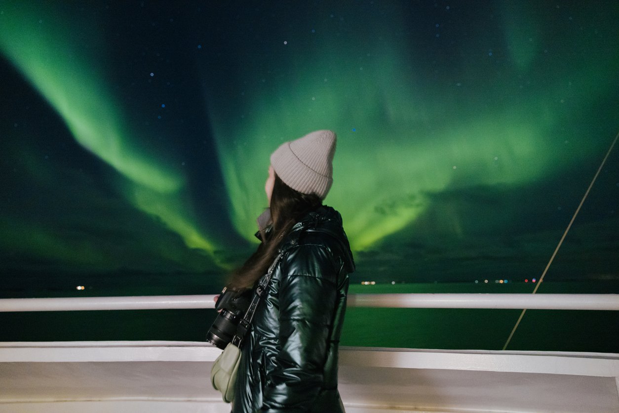 A woman admiring the Northern Lights shining above Northern Norway from a cruise ship