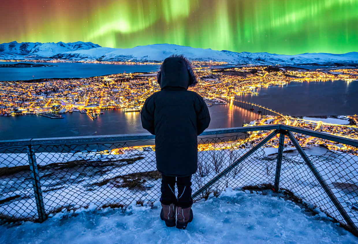 A woman admiring the Northern Lights shining above Tromso, Norway, behind a fence