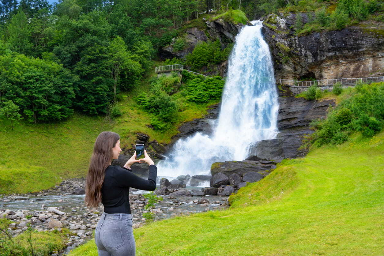 Woman photographing Steindalsfossen, one of the best day trip destinations from Bergen, Norway